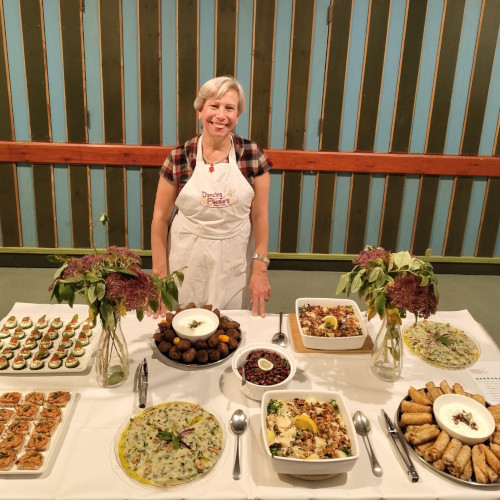 A woman standing next to a large table of Lebanese food